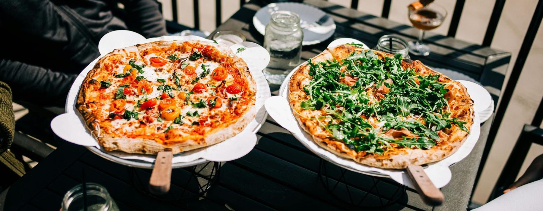 Two people with pizzas at a table outside.